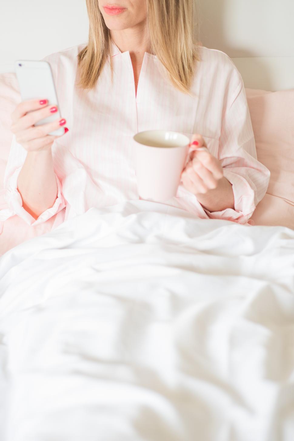 Free Image of Enjoying morning coffee while checking phone in bed 