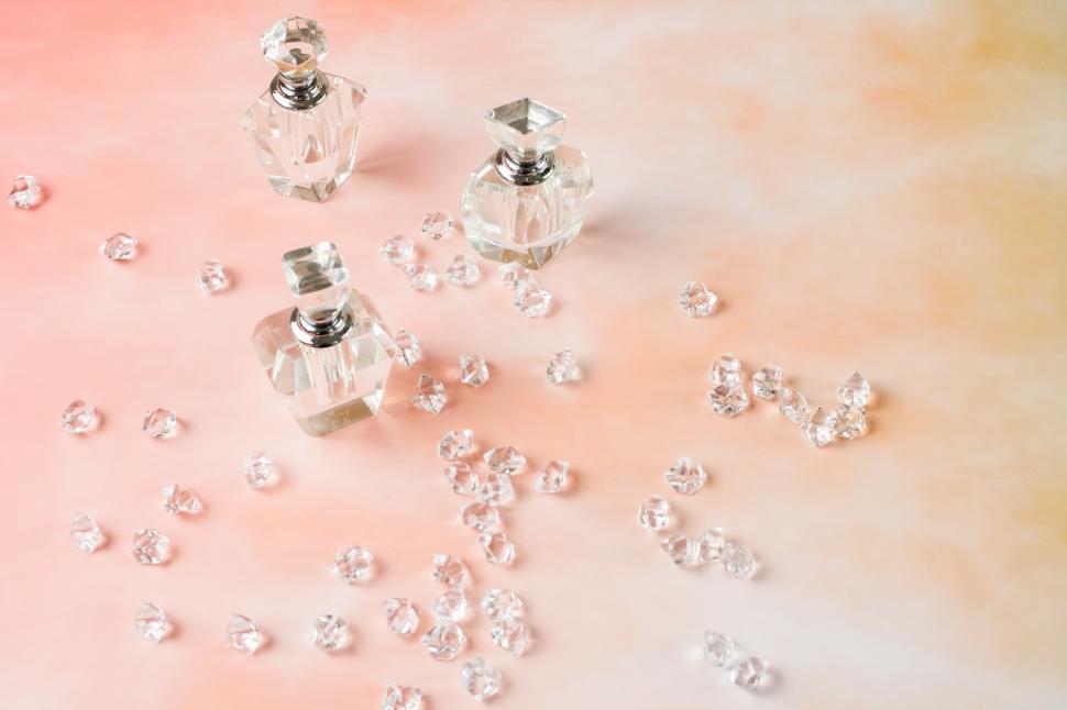 Free Image of Elegant crystal perfume bottles surrounded by shimmering gems on soft pastel backdrop 