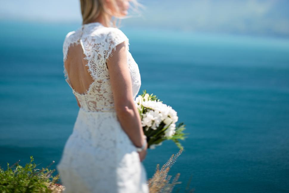 Free Image of Bride in a lace dress by the ocean during a sunny day 