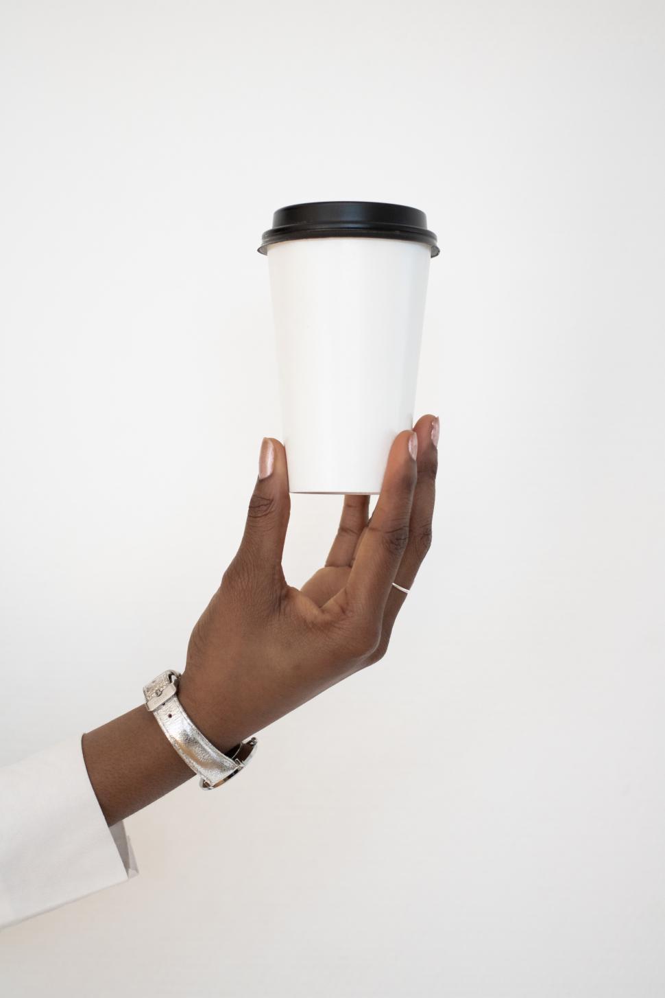 Free Image of Hand holding a white coffee cup against a light background 