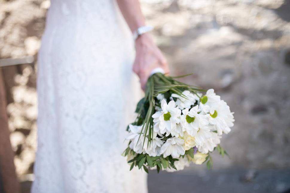 Free Image of Bride holds bouquet of white flowers at outdoor wedding 