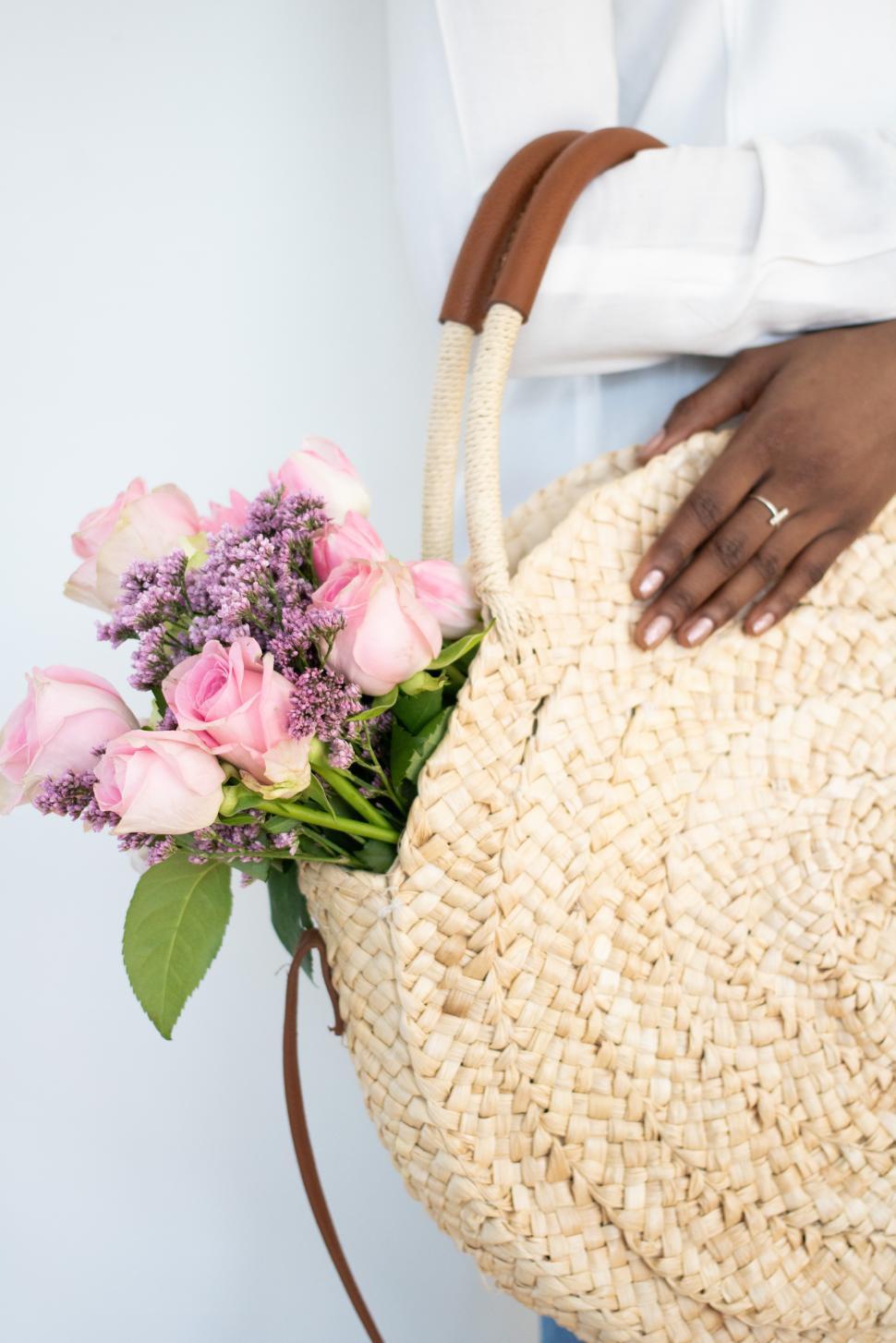 Free Image of Woman holds straw bag with fresh flowers in hand 