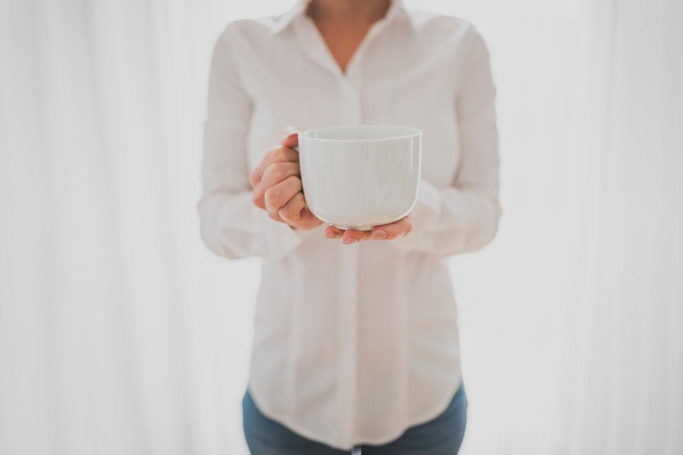 Free Image of Woman holding a white mug in a bright setting 