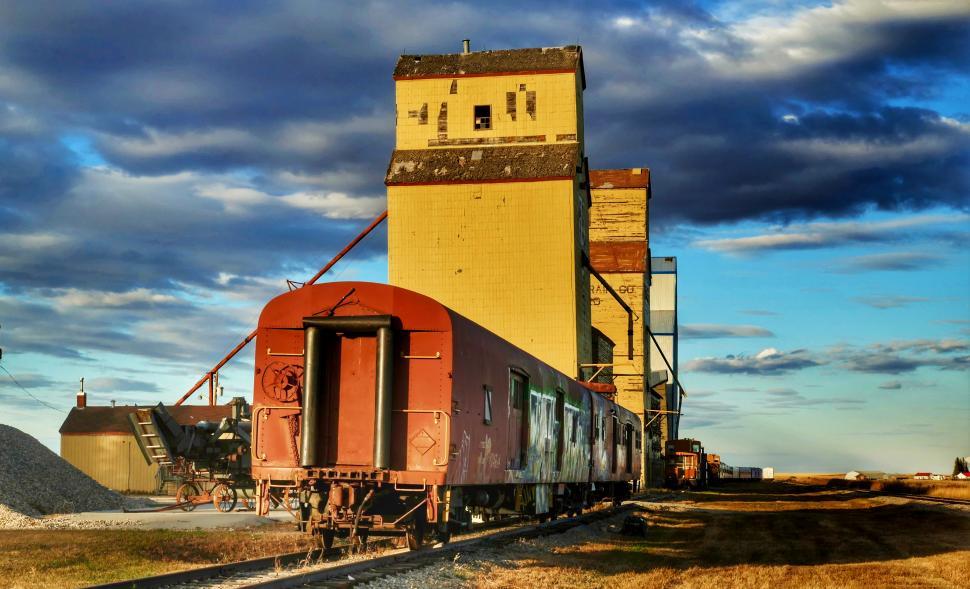 Free Image of Old freight cars beside a grain elevator in rural landscape during sunset 