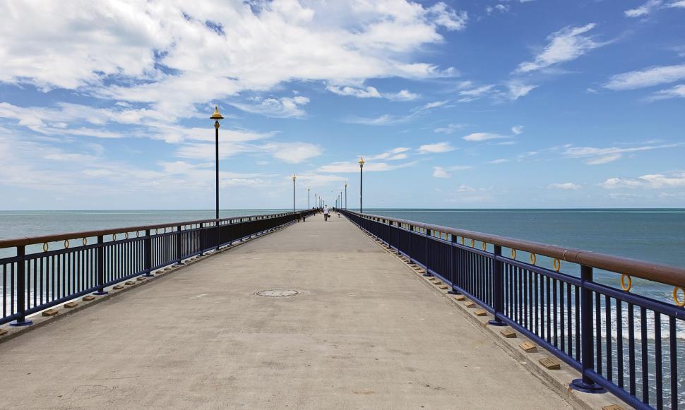 Free Image of Pier extends into calm waters under a bright blue sky with scattered clouds 