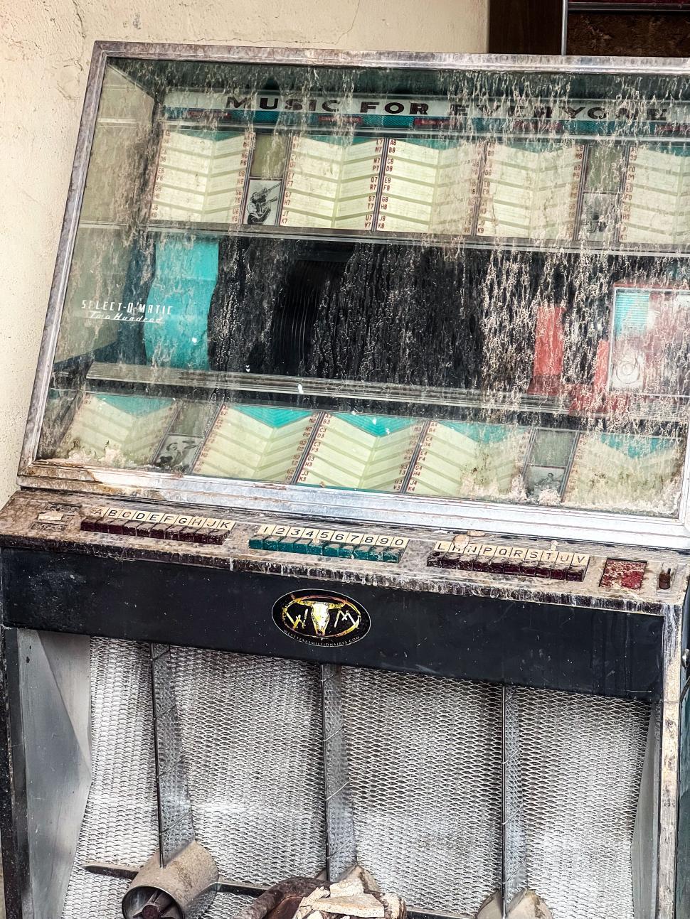 Free Image of Vintage jukebox displayed in a neglected outdoor setting on a sunny day 