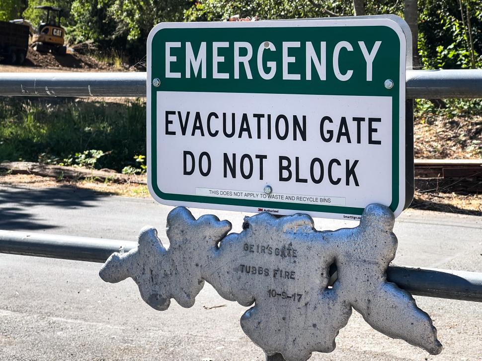 Free Image of Evacuation gate sign displayed prominently near a road in a wooded area 