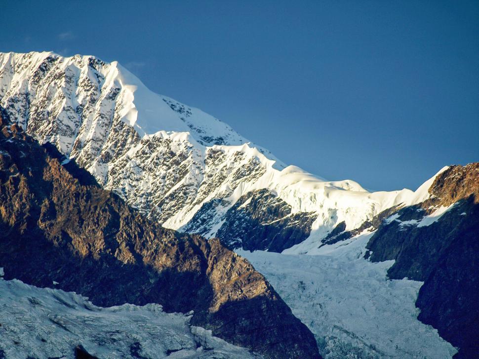 Free Image of Snow-capped mountain peak in bright blue sky above rocky terrain during daylight 