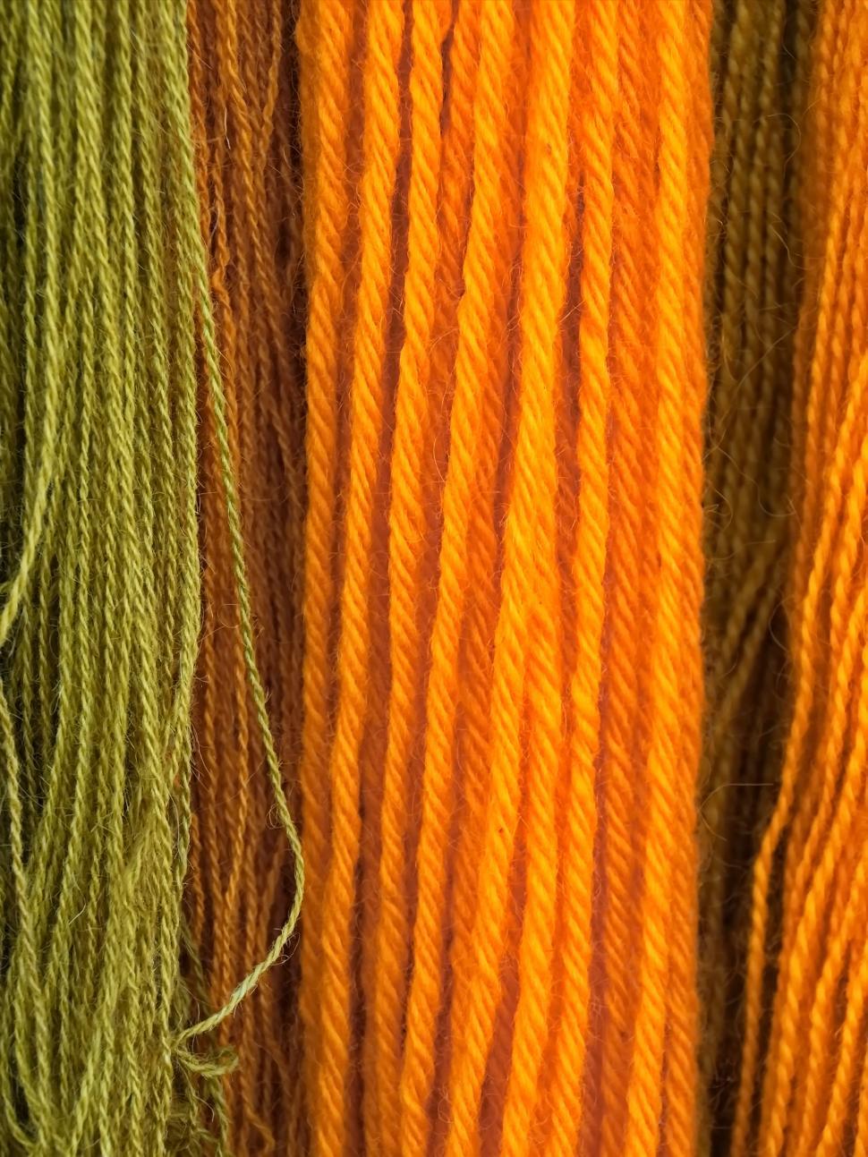 Free Image of Vibrant strands of yarn in shades of green, orange, and yellow arranged neatly 