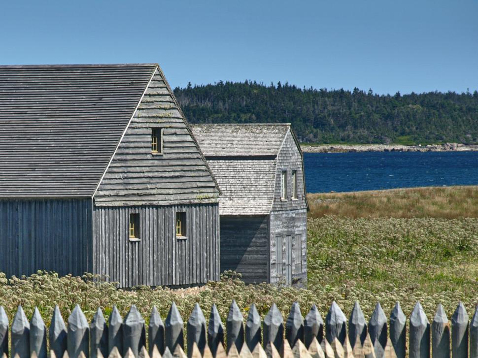 Free Image of Old wooden houses by the coastline with a clear blue sky and distant trees 