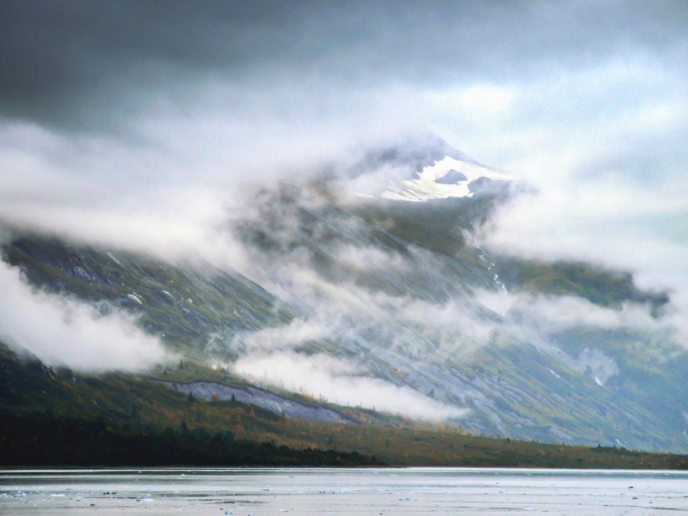 Free Image of Mysterious mountain enveloped in clouds beside tranquil water 
