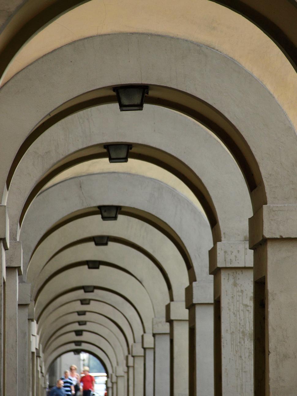 Free Image of Arched walkway with people strolling during sunny day in urban setting 