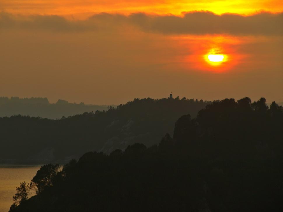Free Image of Sunset over the hills with silhouette of trees and calm water reflection 