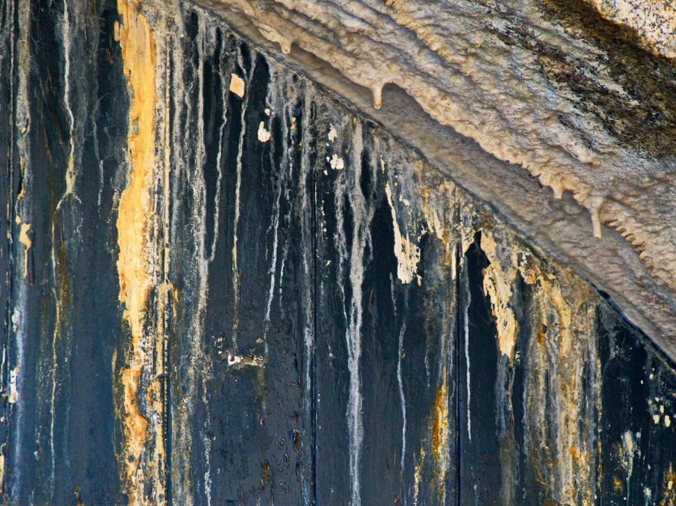 Free Image of Water drips from a weathered structure revealing layers of paint and texture 