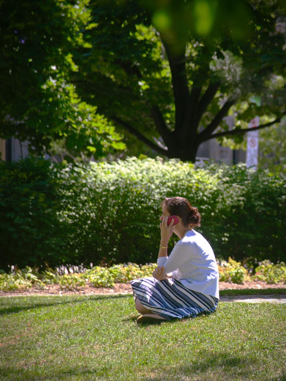 Free Image of Woman sitting on grass talking on phone in a city park during daytime 