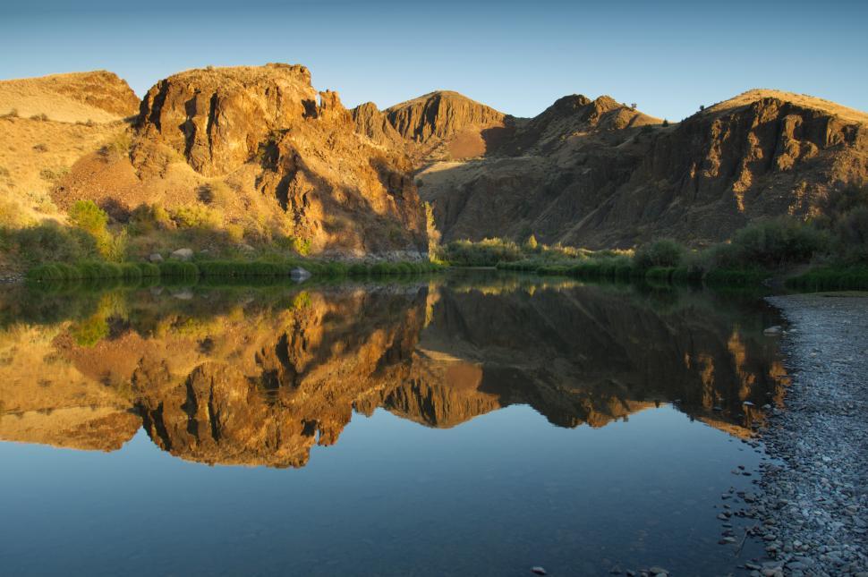 Free Image of Calm water reflects rugged mountains at sunset 