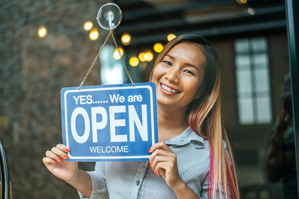 Free Image of woman stands and opens a wide sign through the shop window and smile. 