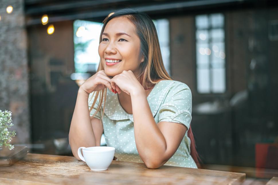 Free Image of The woman is sitting in a coffee shop, putting the chin on the back of the hand and having a cup of coffee. 