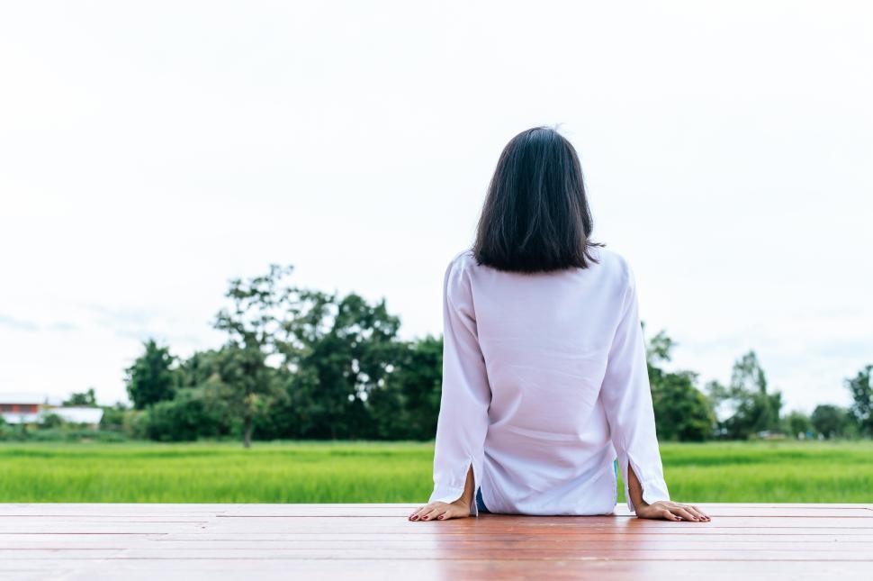 Free Image of woman sitting and relax on Wood bridge with their legs hanging down, taking pictures from behind. 