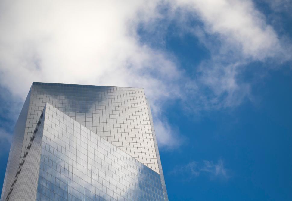 Free Image of Modern glass skyscraper reflecting clouds against a bright blue sky 