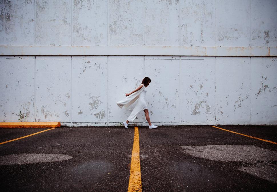 Free Image of Woman in white dress walking on empty parking lot 