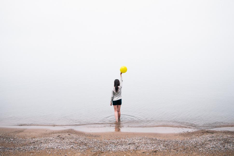 Free Image of Woman holding yellow balloon by foggy lakeside shore 
