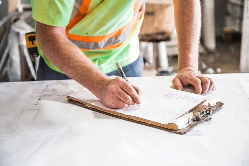 Free Image of Construction worker reviews plans in busy workshop 