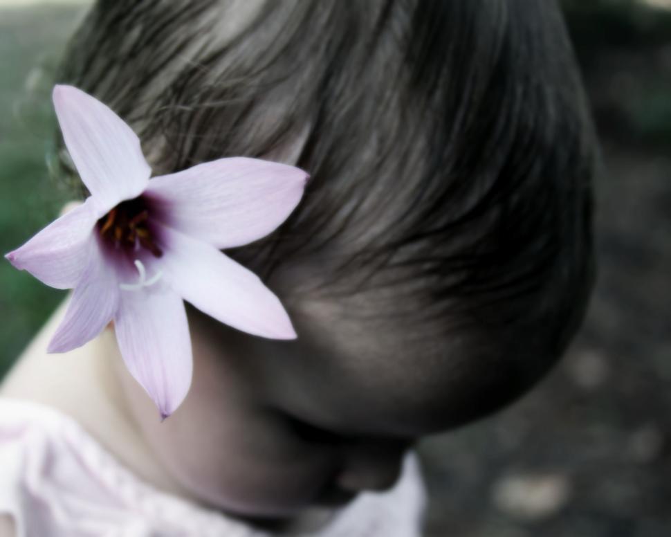 Free Image of Child with pink flower in hair enjoys a peaceful moment outdoors 