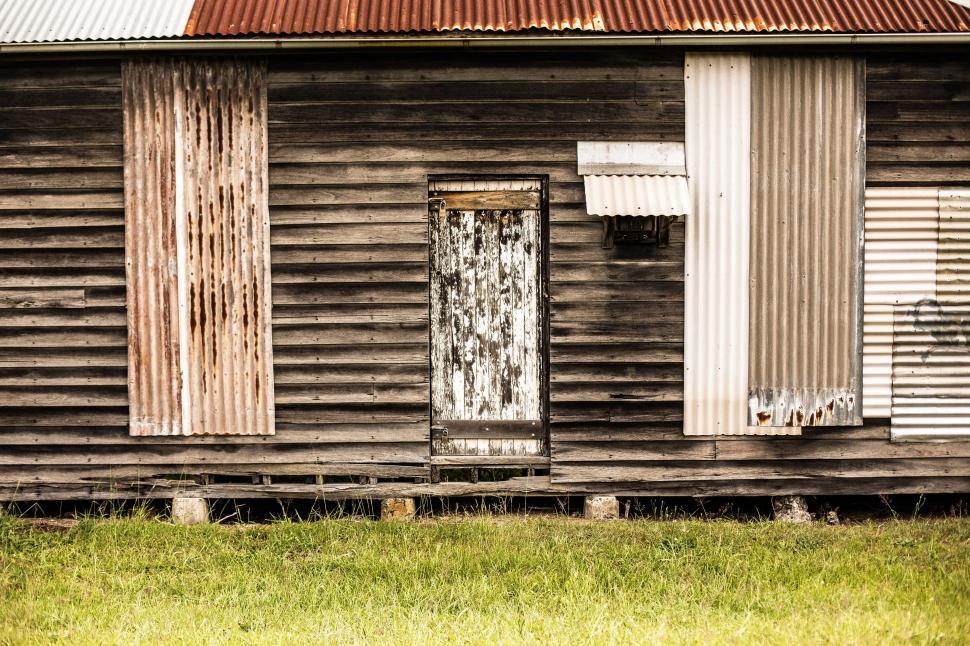 Free Image of Weathered wooden building with rusted metal roof and peeling paint in a grassy area 