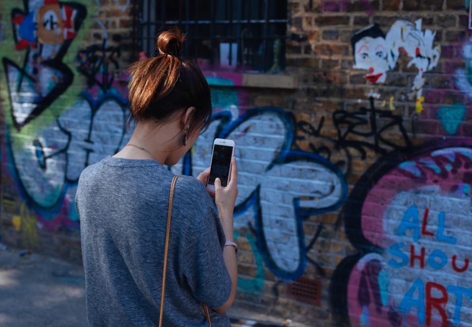 Free Image of Young woman interacts with smartphone in urban art setting 