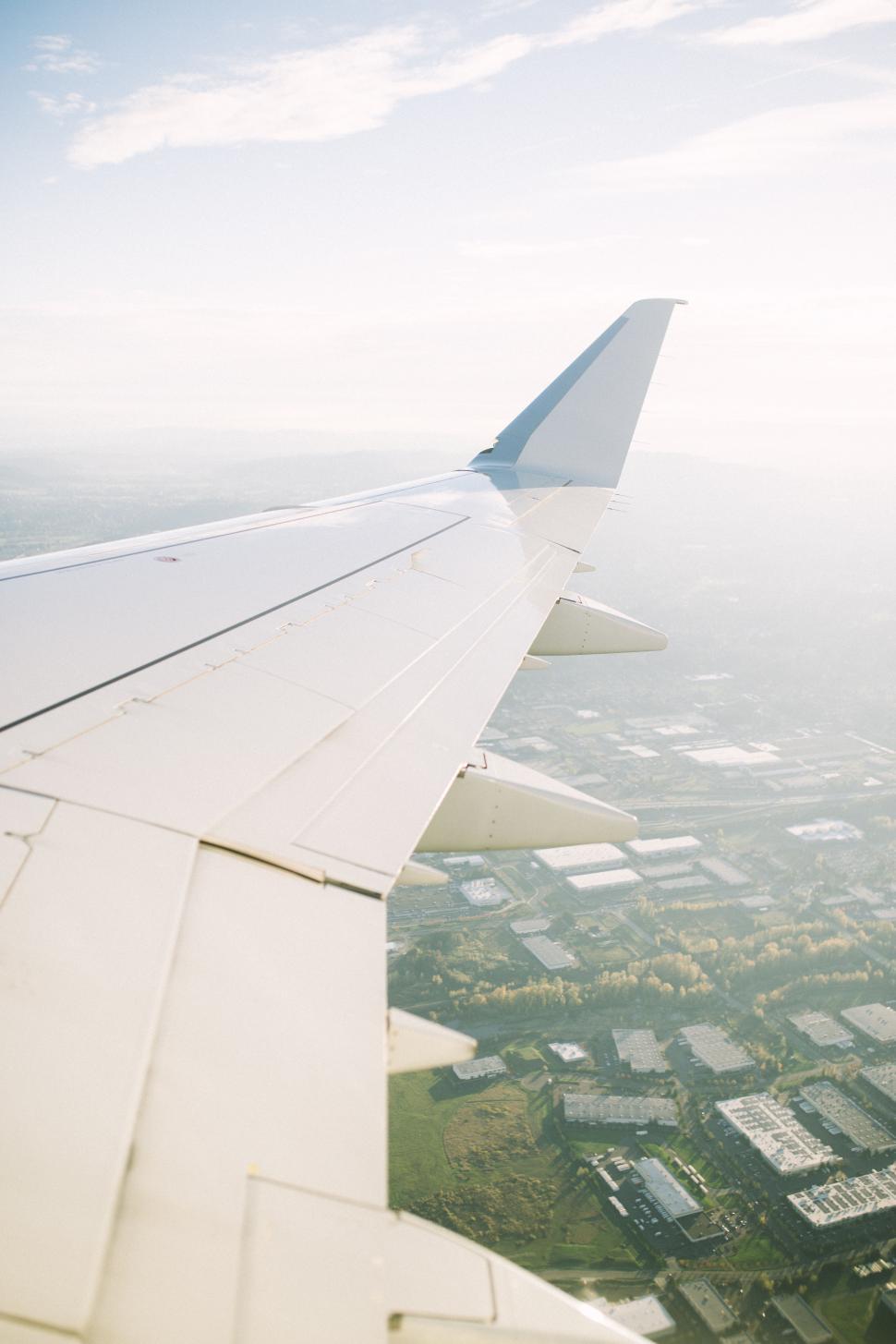 Free Image of View of an airplane wing over green fields and buildings on a clear day 