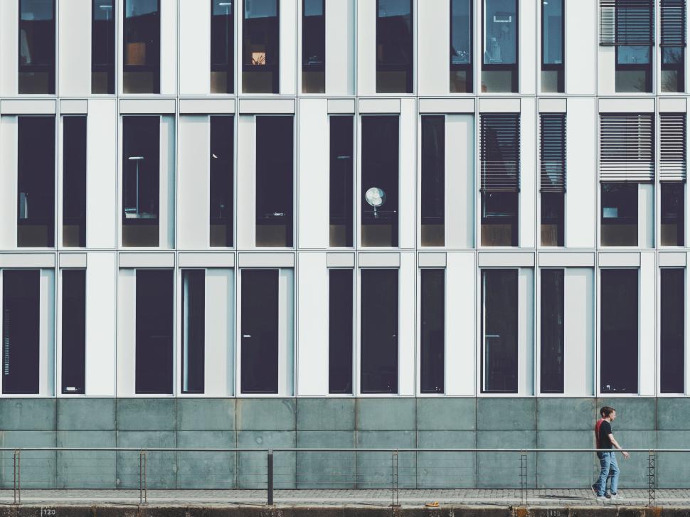 Free Image of Person walking by modern building with large windows in urban setting 