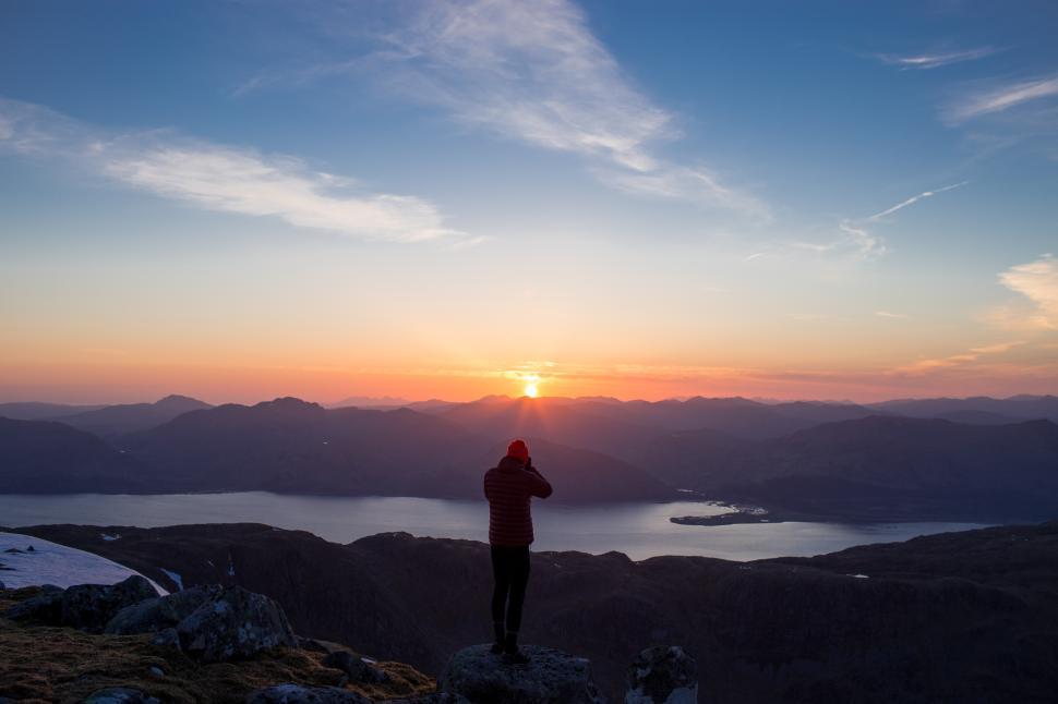 Free Image of Sunset view from mountain peak with silhouetted figure taking photos 