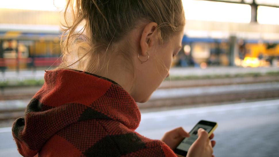 Free Image of Young woman checks phone at train station in daylight 