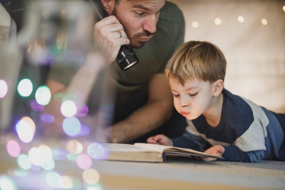 Free Image of Father and son read together by flashlight during cozy indoor evening 