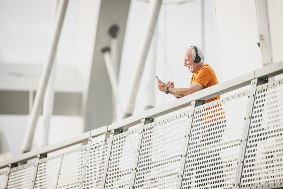 Free Image of Senior man enjoys music while looking at phone on balcony 