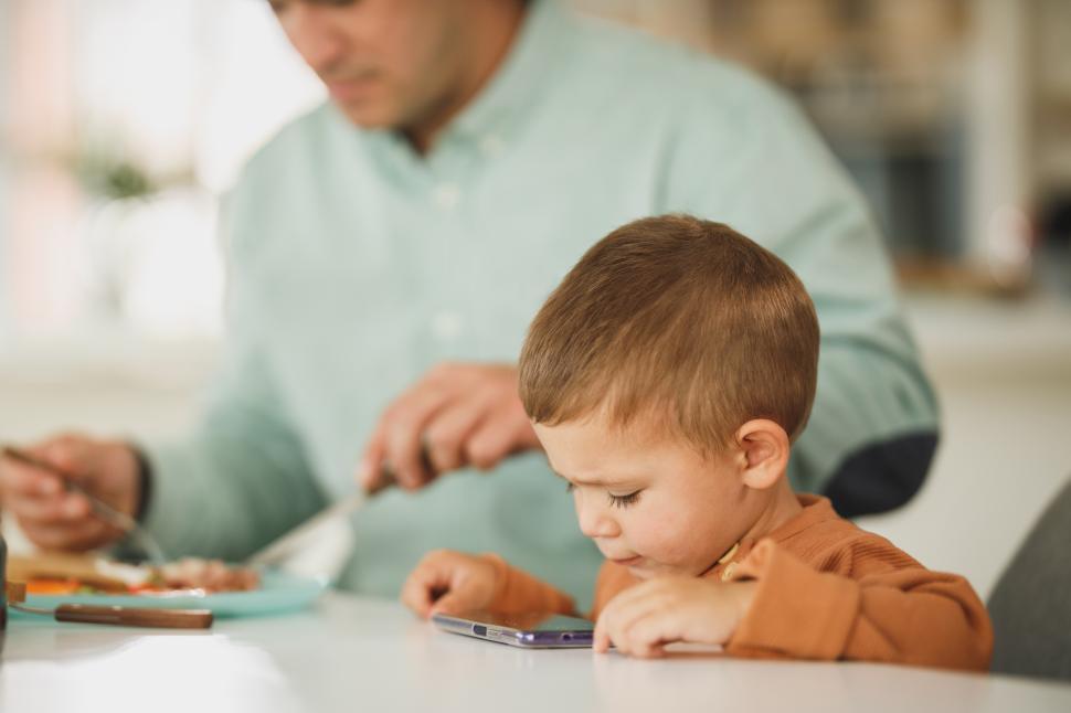 Free Image of Father and son share a meal while the boy plays with a phone 