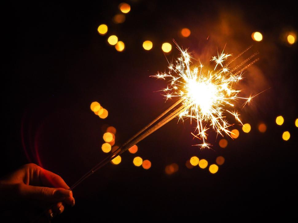 Free Image of Hand holding a sparkler with bright lights in the background during a celebration 