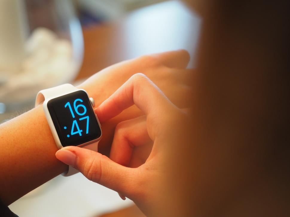Free Image of Woman adjusting smartwatch display while seated at wooden table 