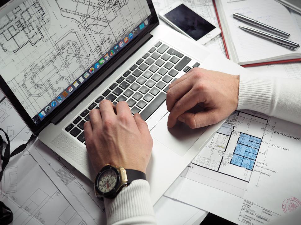 Free Image of Architect reviews blueprints and designs on a laptop in an office space 