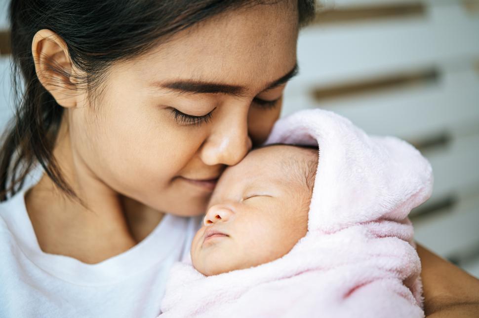 Free Image of The newborn baby sleeping in the mother s arms and fragrant on the baby s forehead. 