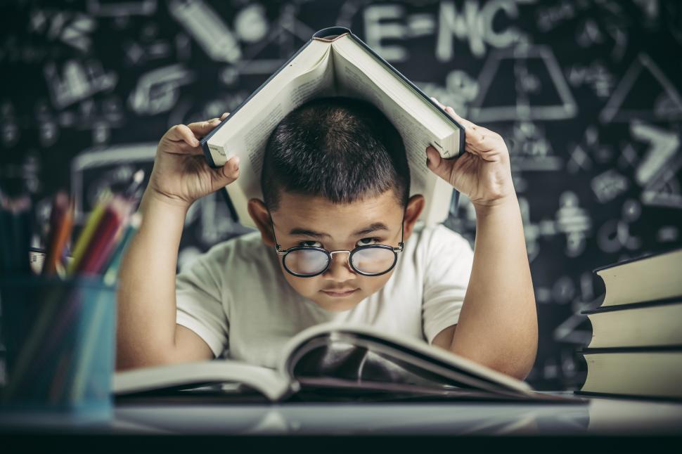 Free Image of A boy with glasses studied and put a book on his head in the classroom. 
