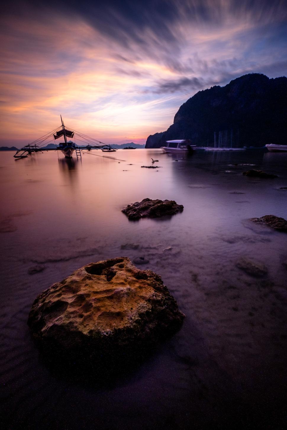 Free Image of Sunset over tranquil waters with boat and rocky shore 