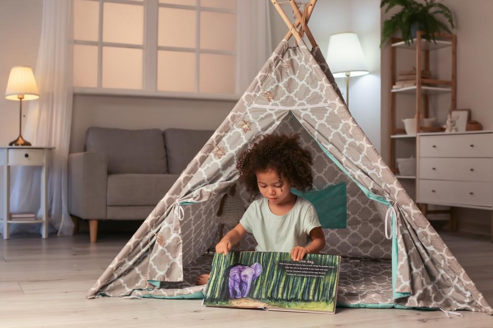 Free Image of Child reads book inside cozy tent in living room during afternoon 