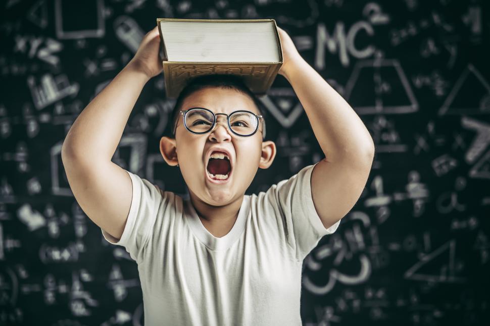 Free Image of A boy with glasses studied and put a book on his head in the classroom. 