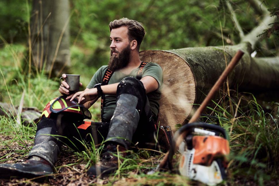 Free Image of Forest worker enjoying a break while seated on a log with tools nearby 