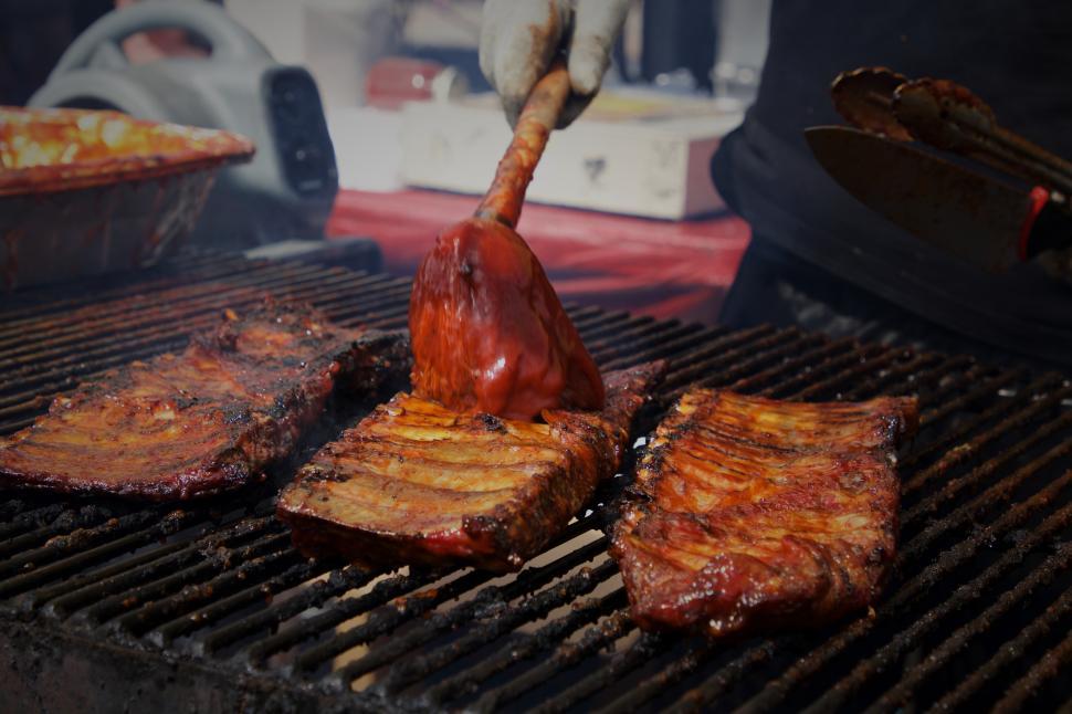 Free Image of Juicy grilled ribs being basted with sauce at a summer barbecue gathering 