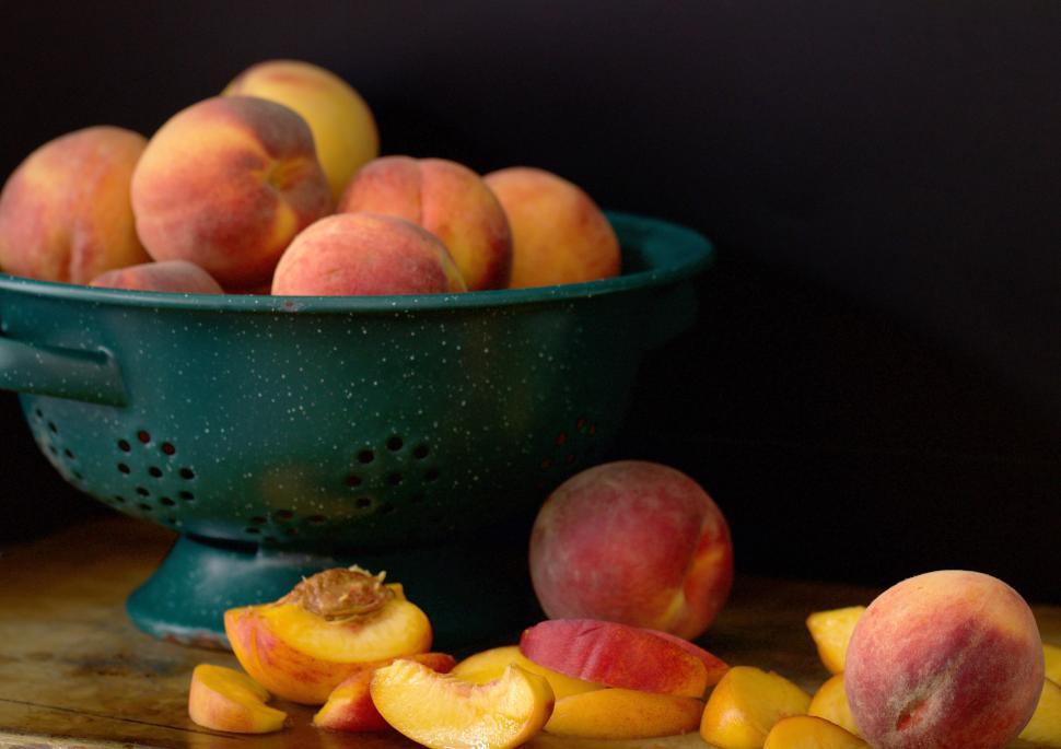 Free Image of Fresh peaches displayed in a green colander on wooden table 