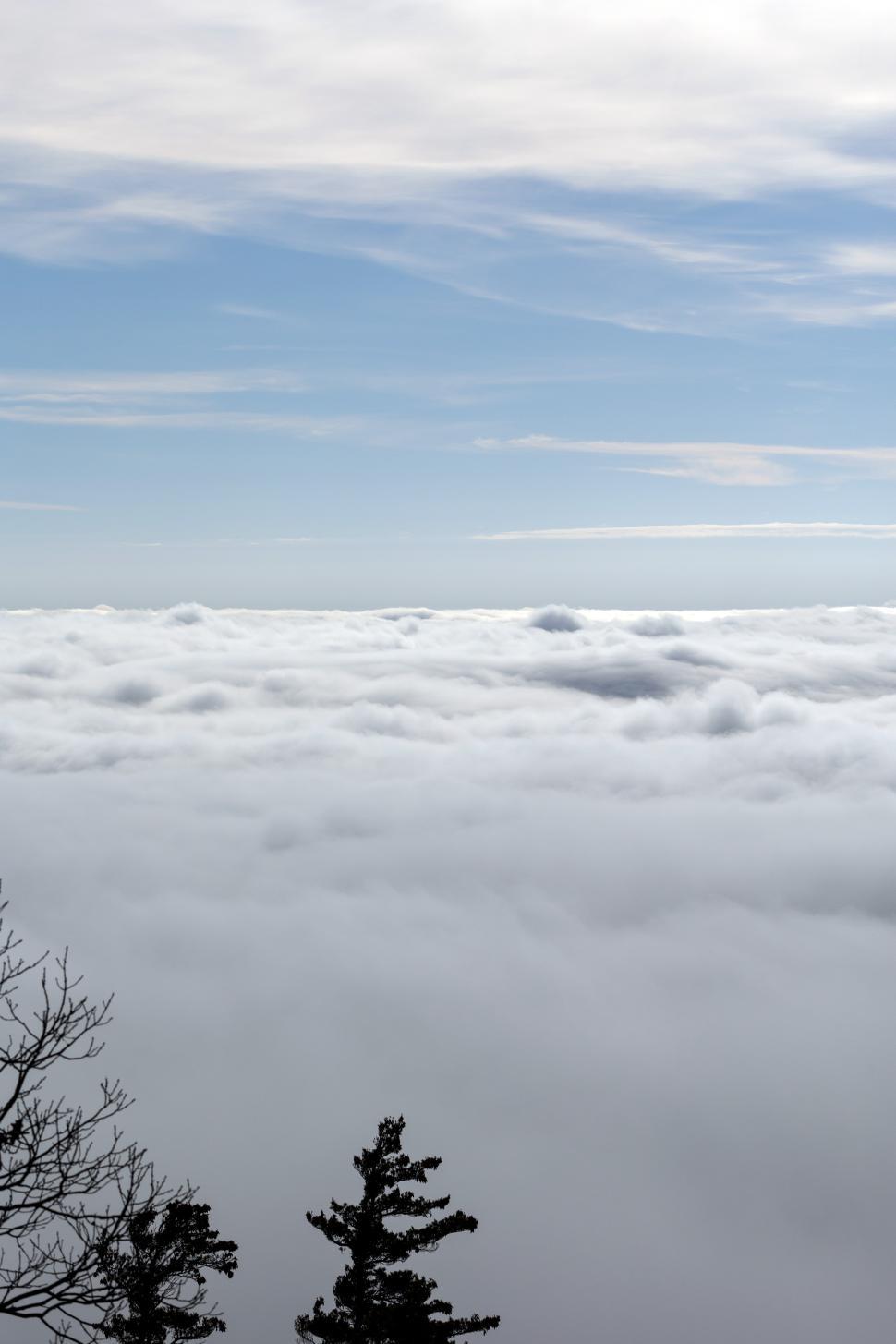 Free Image of Cloudscape over mountain range with clear blue sky and distant trees 