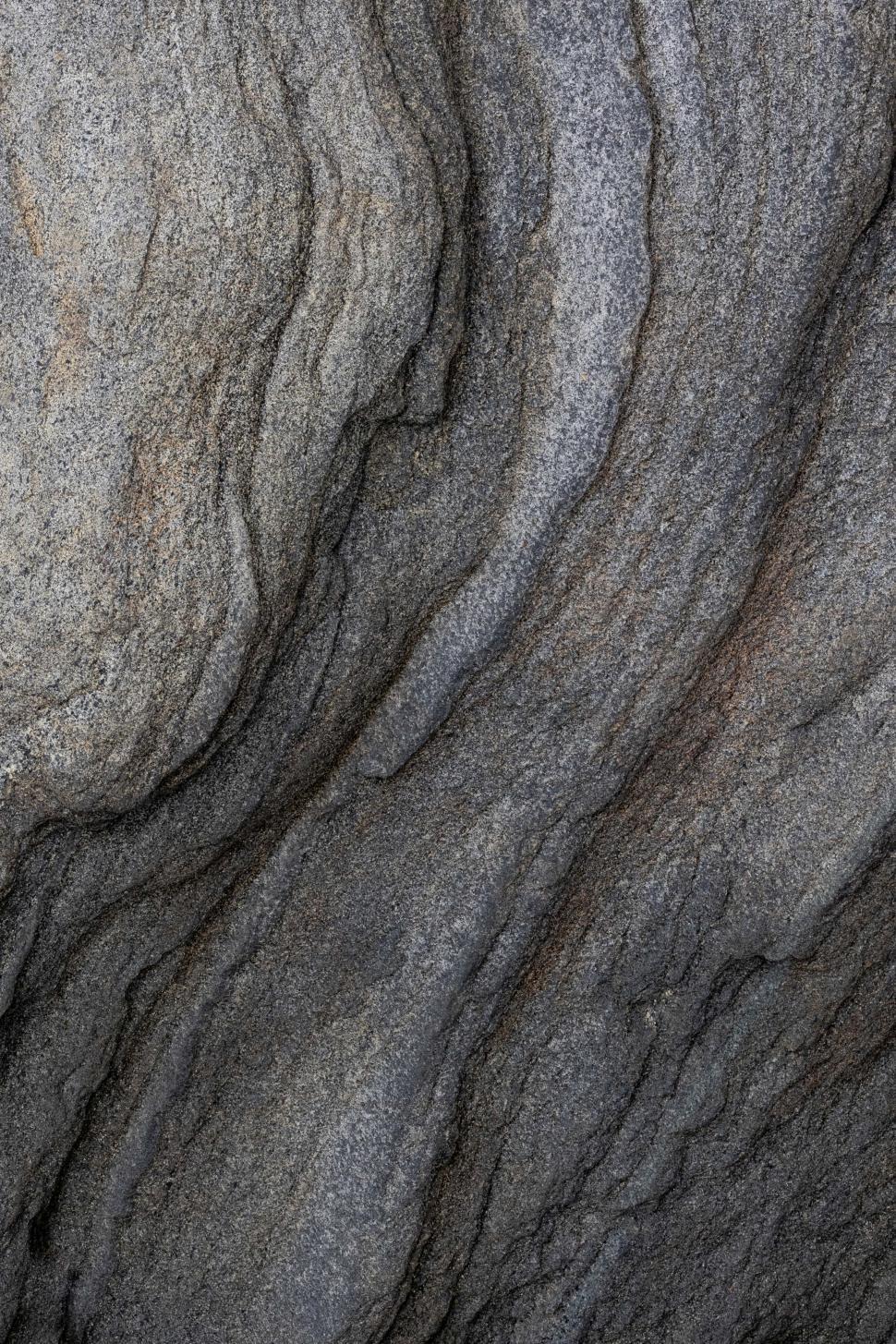 Free Image of Gray textured rock formation with layers and waves visible in nature setting 